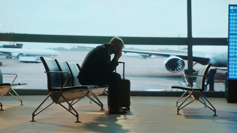 Frustrated guy at an airport with his face in his hands