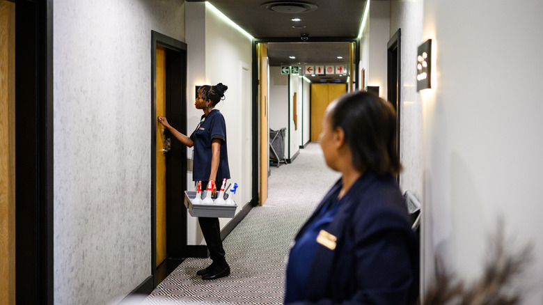 For safety reasons, a supervisor keeps watch as a young housekeeper is about to enter a room