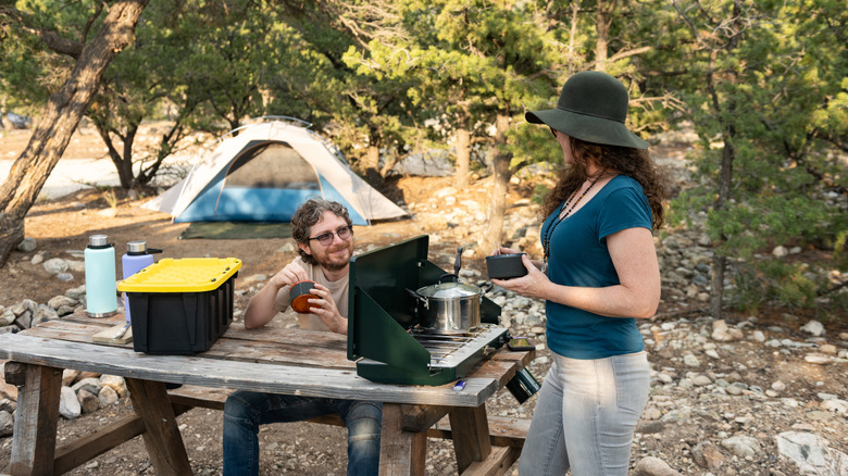 A couple cooking on a portable camping stove in a campground