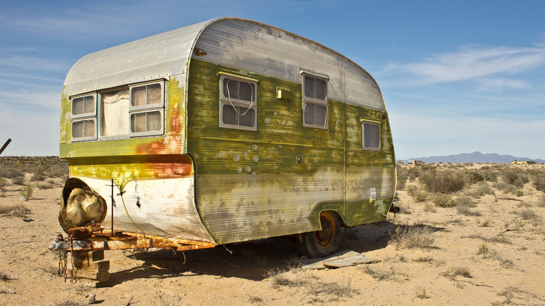 A very old, dirty trailer parked in the desert