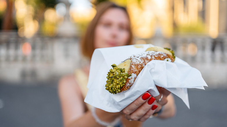 A woman holding a cannoli in a napkin