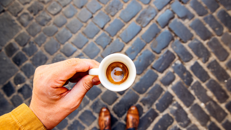 Espresso being held against a cobblestone background