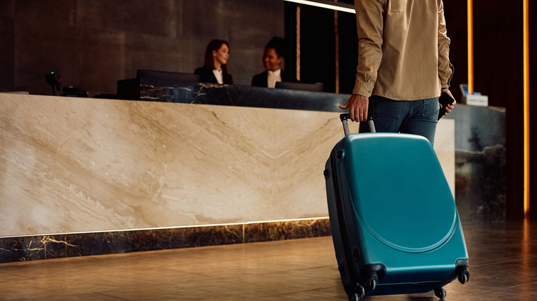 Person walking up to hotel desk rolling suitcase