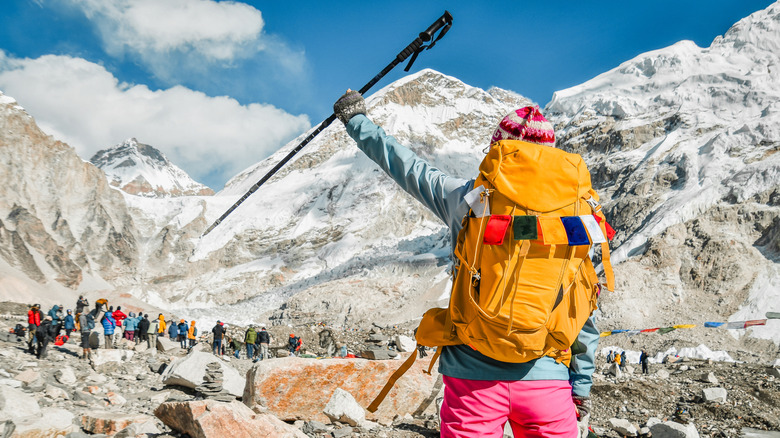 The back of a hiker and her backpack as she raises a climbing pole at the base of Mount Everest