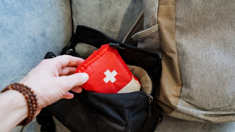 A person places a small first aid kit bag into a travel pack