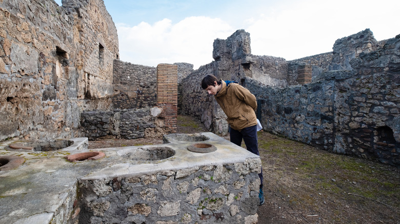 Boy looking into an ancient thermopolium counter in Pompeii ruins