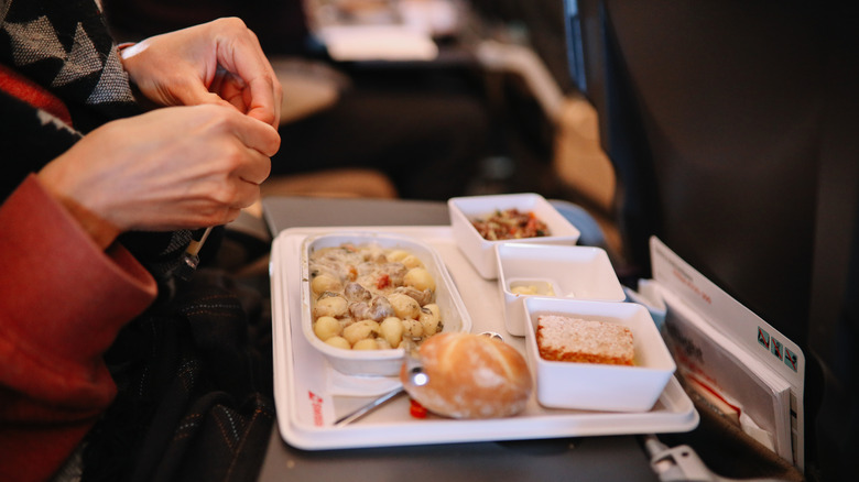 Close-up of a passenger's food tray with pasta, bread, and dessert.