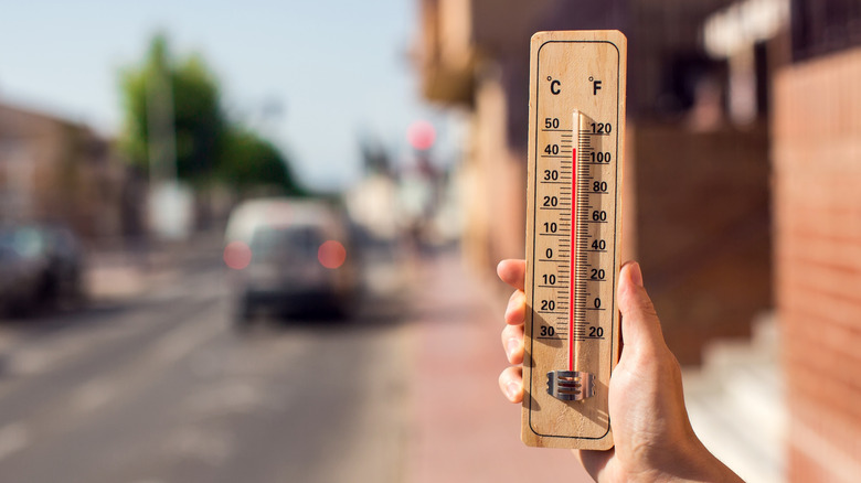 hand in urban environment holding thermometer reading over 100 degrees Fahrenheit