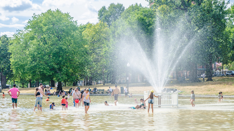 people cooling off under a fountain in a city park on a hot day