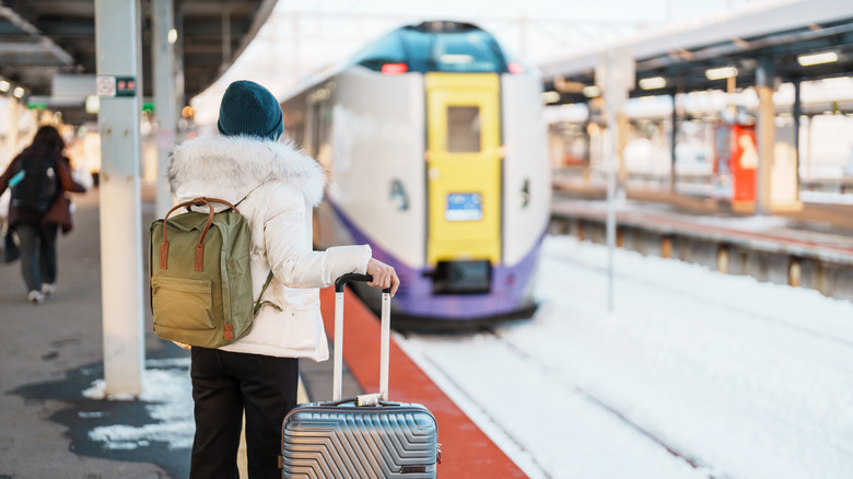 A woman traveler with backpack and luggage watching a train pulling up to the station