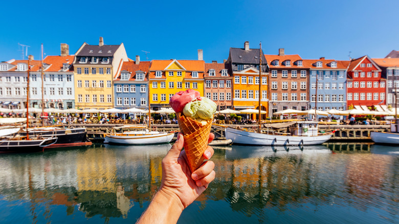 Hand holding an ice cream cone infront of colorful buildings in a coastal European city.