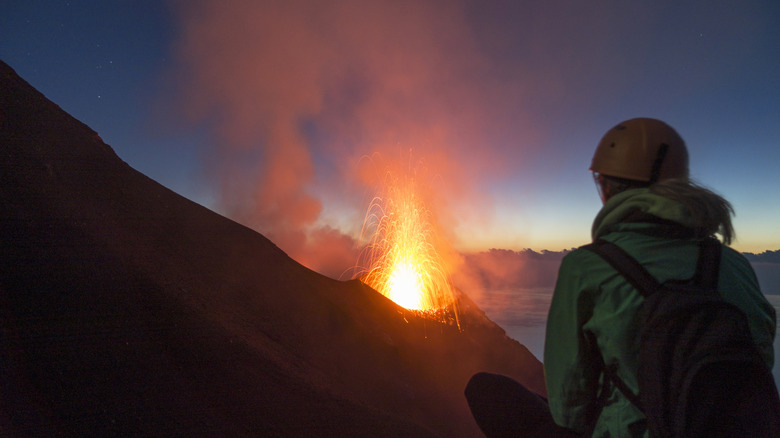 Hiker with a helmet watches volcanic eruption at Mount Stromboli