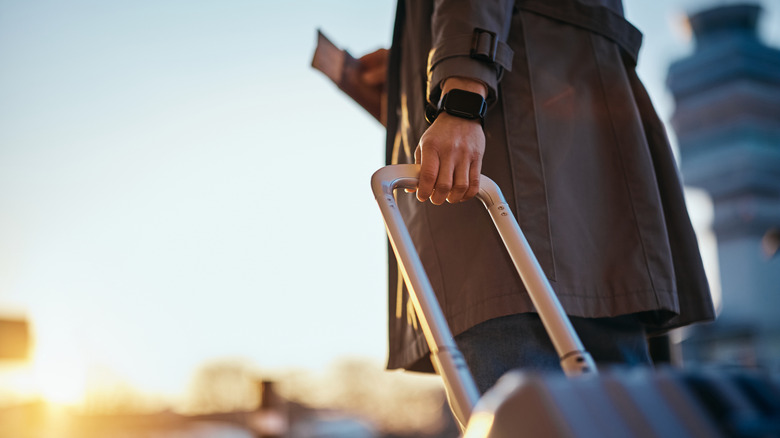 Close up of woman carrying a passport and handle of carry on luggage