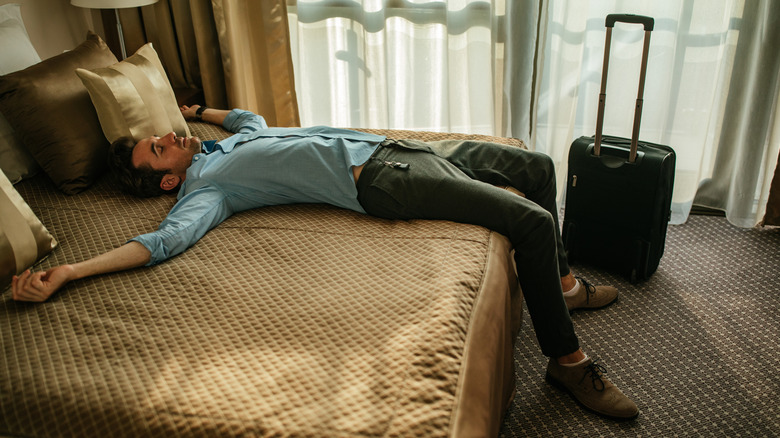 Exhausted person laying on bed in hotel with suitcase