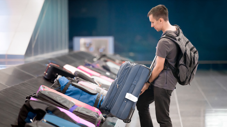 Passenger picking up luggage from baggage claim carousel