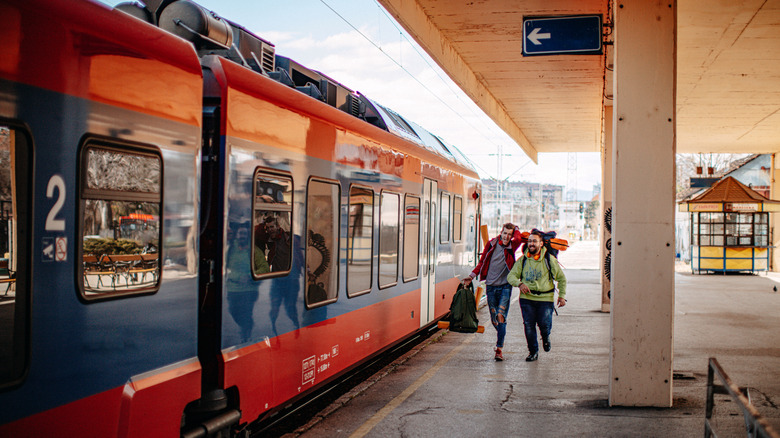 Two men with rucksacks on their backs running toward train on platform