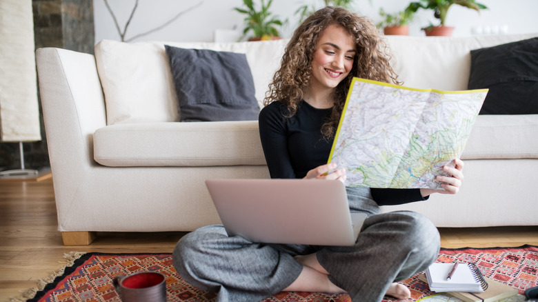 Female traveler planning a trip abroad, looking at a map with laptop open on her knees