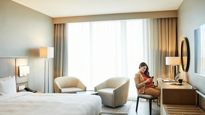A woman dressed in business clothes works on her laptop at a desk in an upscale hotel room