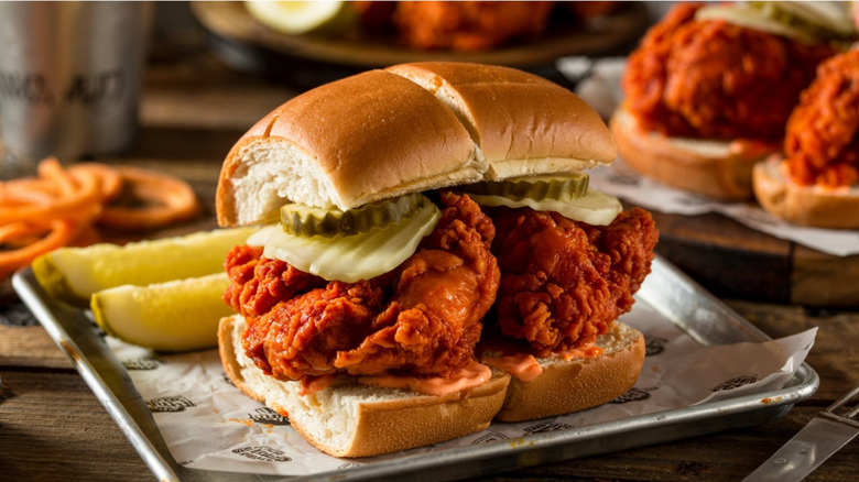 a fried chicken sandwich on a metal tray with pickle spears