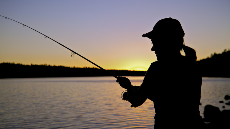 A silhouette of a woman fishing at sunset.