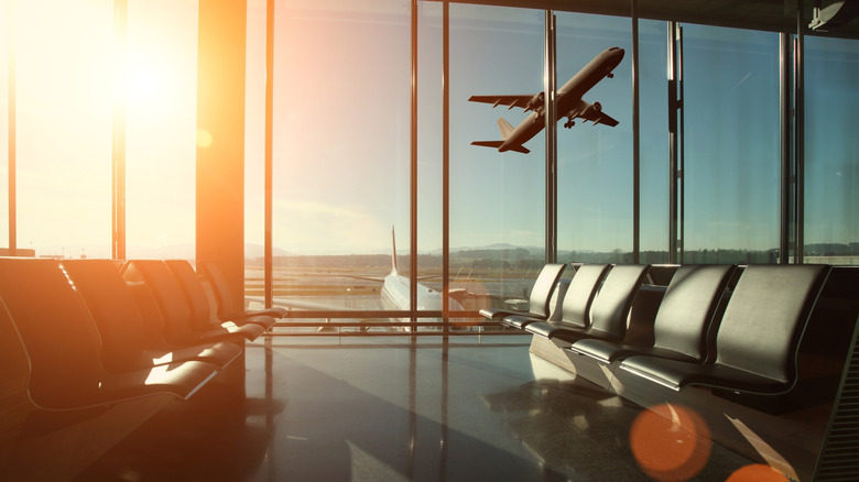 Empty seats in a small airport terminal watching one airplane take off.