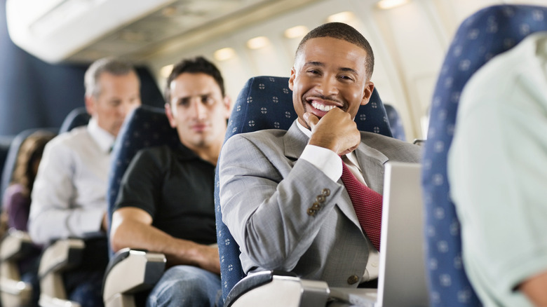A man smiling and using laptop on plane
