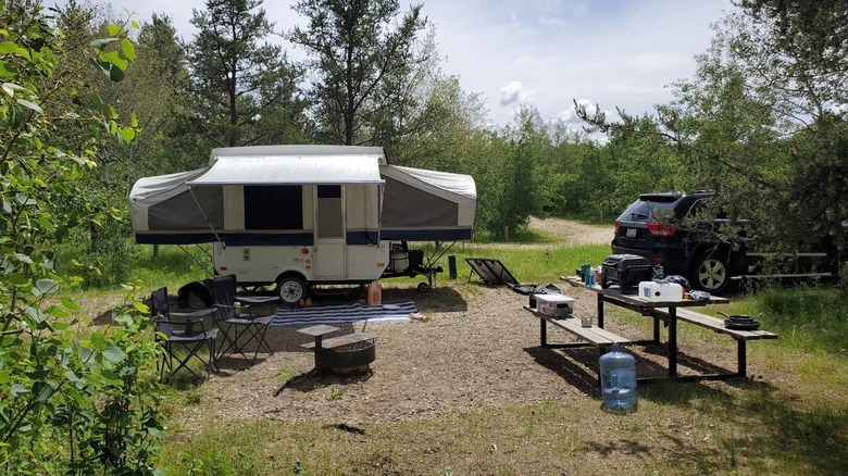 A trailer, camping chairs, picnic table, and SUV sit in a clearing at Whitney Lakes Provincial Park