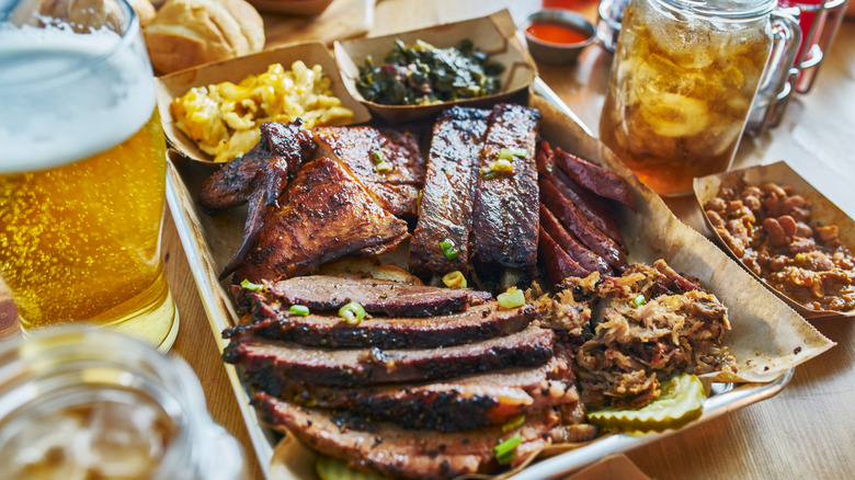A barbecue platter featuring a variety of meats, sides, and beverages