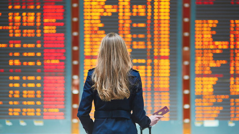 An airport departure board with a woman standing in front of it