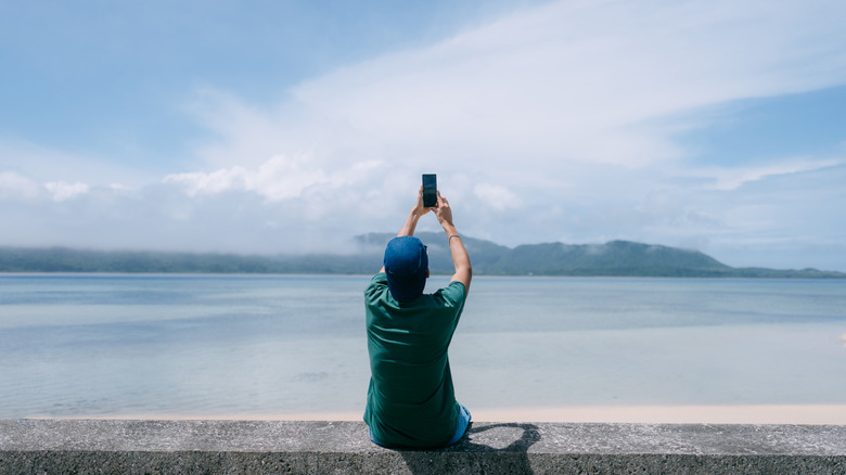 Man taking photo of an island on the horizon with his smartphone