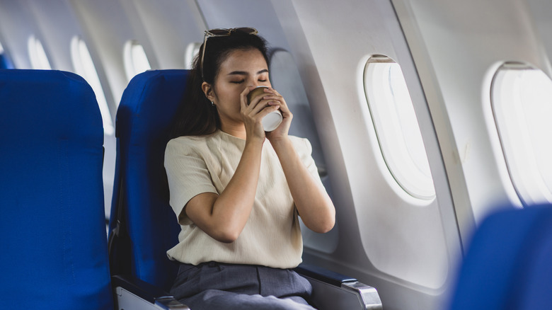 A female plane passenger holds a paper coffee cup to her mouth with two hands