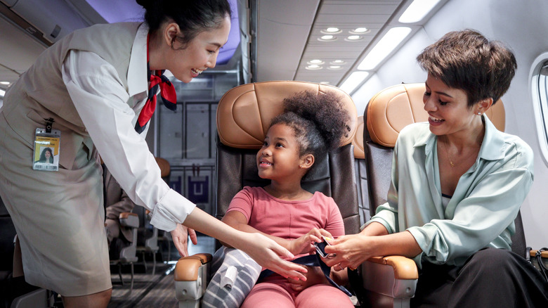 Flight attendant and mom teaching a kid to buckle seat belt on plane