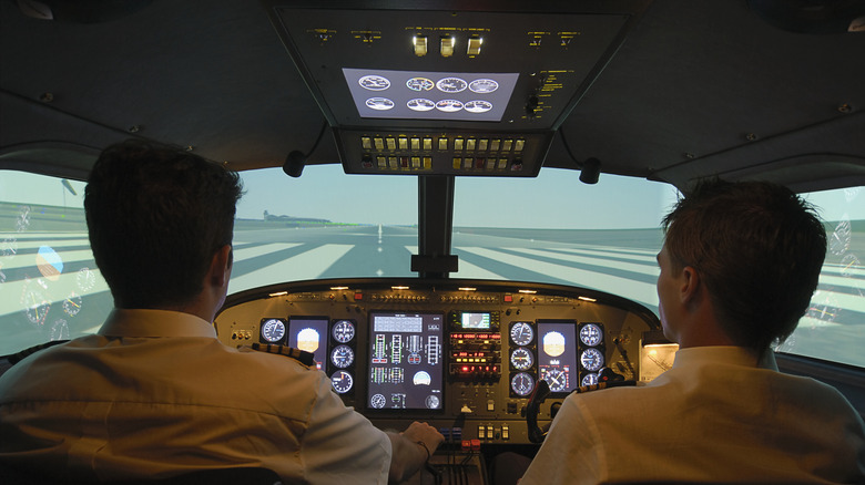 Two pilots sit in a cockpit with a view of the runway