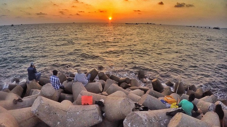Travelers sit on a breakwater in Phú Quốc and watch the sunset over the waves