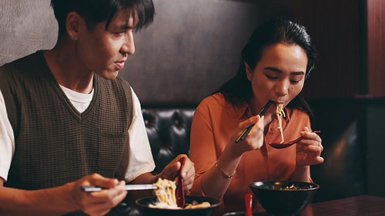 A young Asian couple eating ramen at a restaurant.