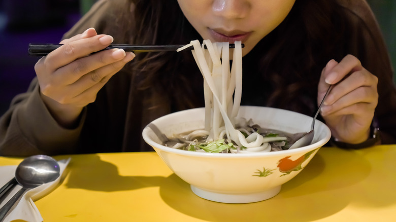 A female diner slurps noodles from a bowl of pho.