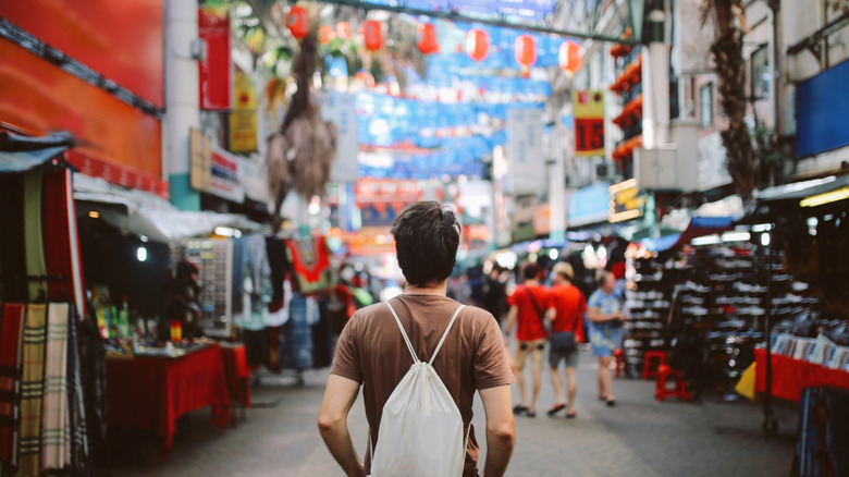 Rear view of a man with sling bag facing a Malaysian street with shops and festive bunting overhead