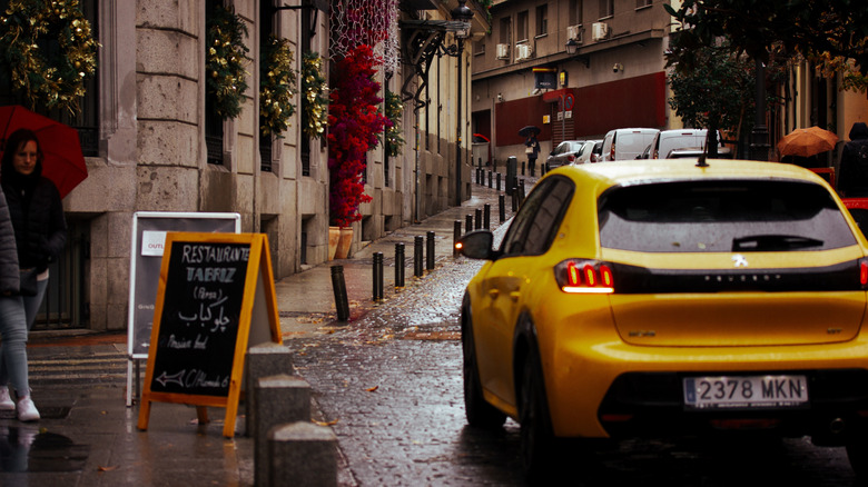 A yellow car navigates the narrow cobbled streets of Madrid on a rainy day