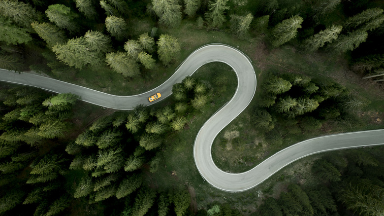 A car can be seen navigating an S-shaped road through a rural, alpine region of Italy