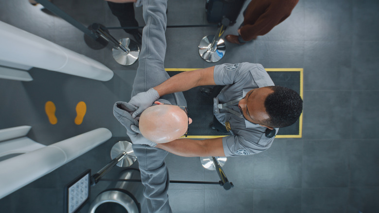 A man wearing a hoodie getting patted down by a TSA agent after his first screening.