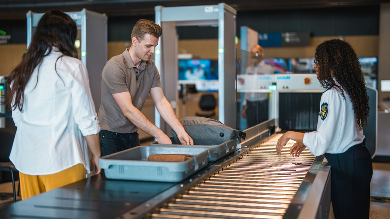 People standing at an airport security checkpoint with plastic bins