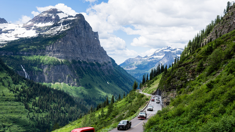 Line of cars on Going-to-the-Sun Road surrounded by snowy mountain peaks and waterfalls