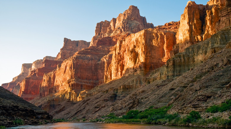 Red cliffs of Grand Canyon in sunlight above the Colorado River with clear blue sky