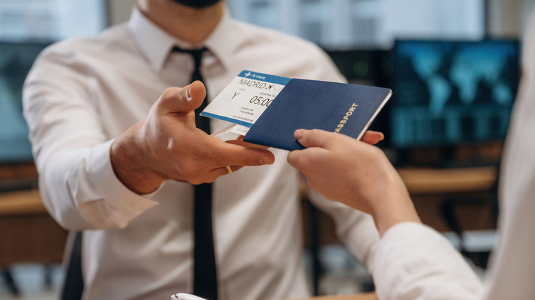 A ticket agent hands a physical boarding pass and passport back to a passenger.