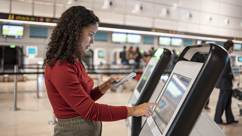 A woman uses an electronic kiosk and her smartphone to check-in at an airport.
