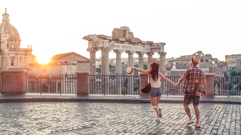 Young couple hand-in-hand with Rome's forum and church dome in backdrop at sunset