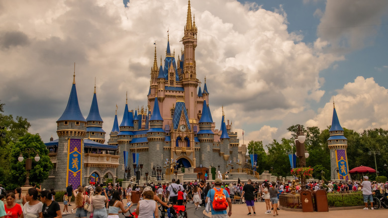 The entrance of Magic Kingdom Park, one of the four theme parks at Walt Disney World in Orlando, with crowds of people all around.