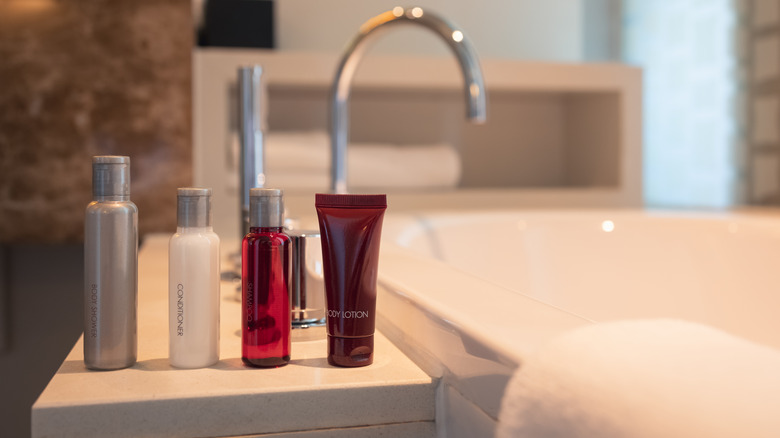 Mini toiletries in single-use plastic bottles lined up next to a bathtub