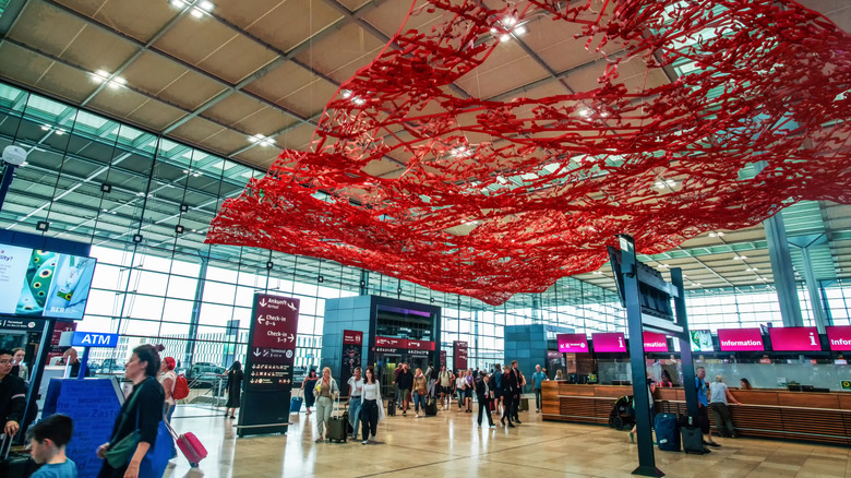 Interior of Berlin Brandenburg Airport with travelers walking by and red artwork on the ceiling