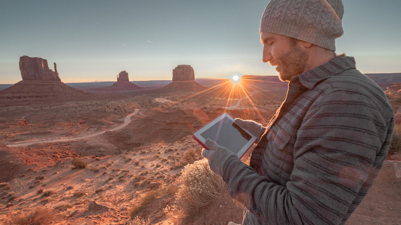 A man stares at a tablet in Monument Valley, Utah, as the sun peeks over the horizon